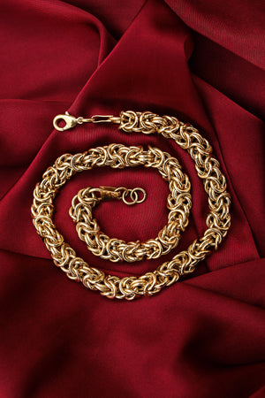 Gold chain necklace with intricate interwoven links, elegantly displayed on rich red satin fabric.