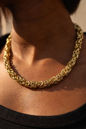 Gold chain necklace with intricate interwoven links, elegantly worn