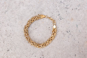 Gold chain bracelet with intricate interwoven links, elegantly displayed on rich red satin fabric
