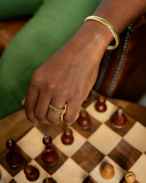 Hand with a gold ring and bracelet on a chessboard