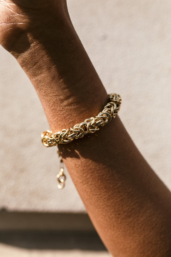 Gold chain bracelet with intricate interwoven links, elegantly displayed on a wrist 