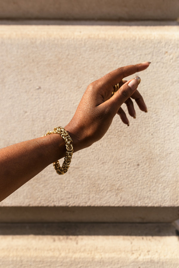 Gold chain bracelet with intricate interwoven links, elegantly displayed on a wrist 